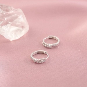 Silver twisted hoop earrings with pavé zircons on soft pink silk background
