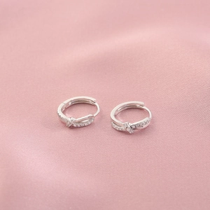 Elegant twisted silver hoop earrings with shimmering zircons on a soft pink silk fabric