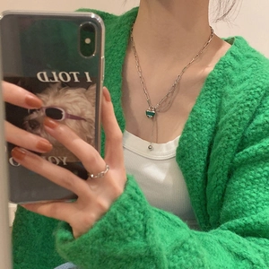 Détail d'un collier chaîne trombone argenté avec pendentif cœur vert et une bague