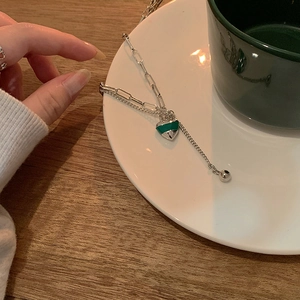 Détail du pendentif cœur vert sur double chaîne argentée posé sur une assiette en céramique blanche