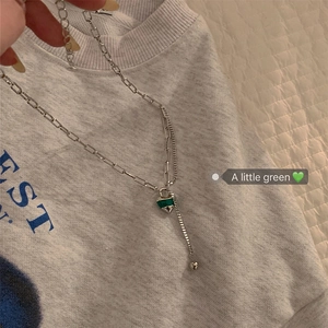 Détail du collier à double chaîne argentée avec un pendentif cœur vert sur maillon trombone