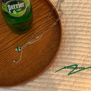 Détail d'un pendentif cœur à rayures vertes sur une chaîne trombone dans un plateau bois