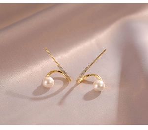 Détail de boucles d'oreilles spirales dorées avec perles et zircons sur tissu satiné