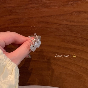 Detail of hand-held silver heart earrings with shimmering zircon pavé on wood background