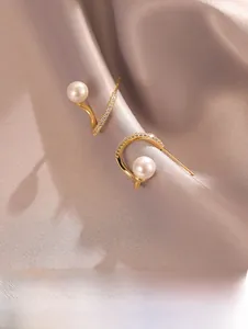 Détail de boucles d'oreilles clips perles dorées en S sur fond de soie de luxe