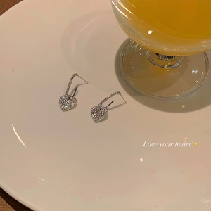 Detailed view of silver heart earrings with white zircons on a white ceramic plate