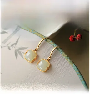 Macro-detail van matgematte gouden oorbellen met vierkante Hetian-jade en lotusontwerp