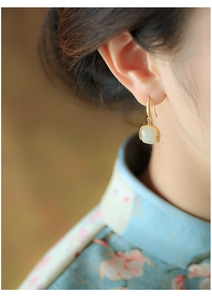 Detailopname van Hetian jade oorbellen met gouden afwerking op model in cheongsam jurk