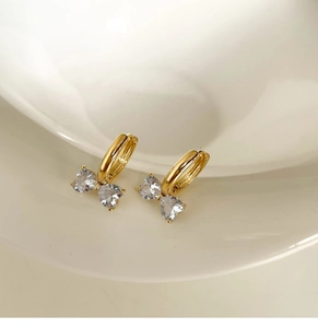 Details von goldenen Huggie-Ohrringen mit herzförmigen Zirkoniasteinen als Schmetterling