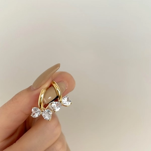 Detail von goldenen Schleifen-Ohrringen mit herzförmigem Zirkonia in der Hand