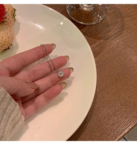 Détail d'un collier argenté avec pendentif en zircon clair posé sur une assiette