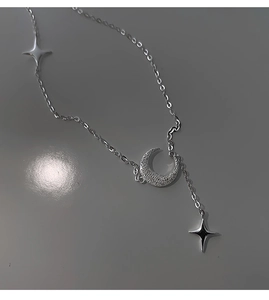 Dettaglio della collana d'argento con ciondolo luna e stelle e trama satinata su grigio