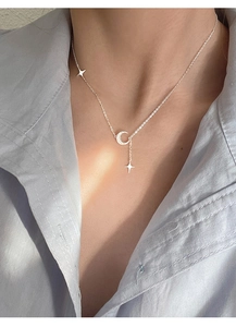 Dettaglio di una collana con pendente a luna e stella indossata su camicia azzurra