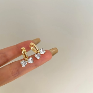 Elegante goldene Schleifenohrringe mit herzförmigen Zirkonia-Kristallen an den Fingern