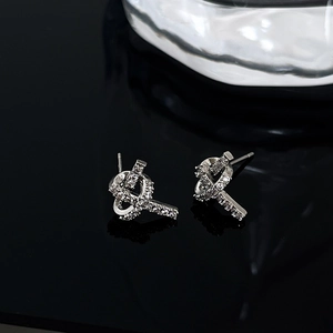 Macro detail of silver knot stud earrings with pave-set zircon crystals on black surface