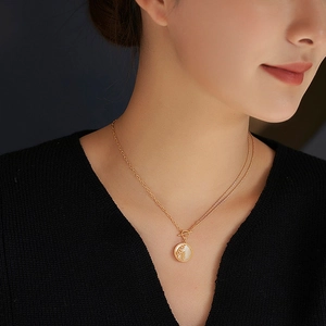 Collier double rang doré avec pendentif rond en nacre porté par un mannequin