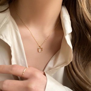 Detailed close-up of golden hollow square pendant necklace on beige satin shirt
