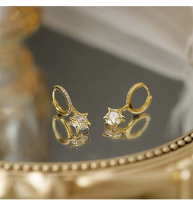 Makrodetail von goldenen Sternanhänger-Ohrringen mit Zirkonia auf Spiegelfläche