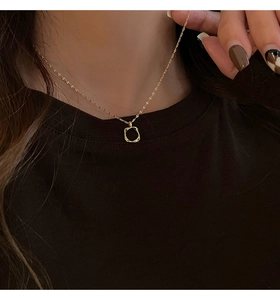 Minimalist gold necklace with irregular square pendant worn on a woman's neck