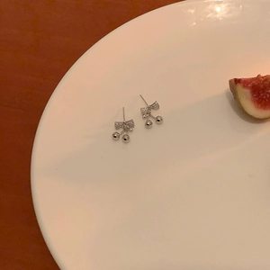 Detail view of silver cherry bow earrings with rhinestones on a white ceramic plate