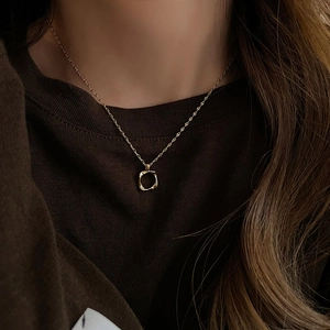 Close-up of a gold minimalist twisted geometric pendant necklace on a female model