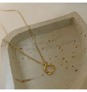 Macro shot of gold hollow square pendant with textured edges on a minimalist chain