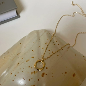 Detailed macro of gold square hollow pendant on polished stone highlighting metallic texture