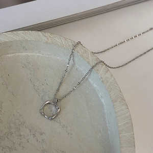 Close-up of a minimalist hollow square pendant necklace in silver on a textured tray