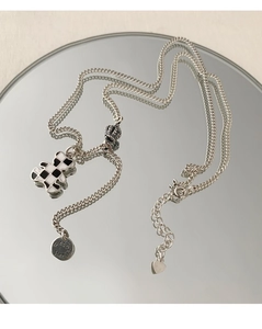 Detail of bear checkered pendant necklace with lucky star tag and crown charm on mirror