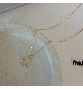 Detail shot of golden necklace with irregular geometric square pendant on stone tray