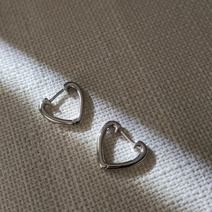 Boucles d'oreilles créoles cœur argentées polies sur tissu beige avec lumière douce