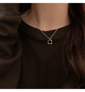 Detail of a gold hollow square pendant necklace worn by a model in a close-up view