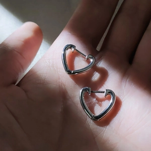 Boucles d'oreilles créoles cœur argentées minimalistes tenues en main sous le soleil