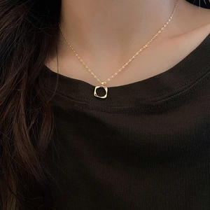 Close-up of a hollow wavy square gold pendant necklace worn by a model in black
