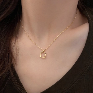 Macro detail of a minimalist gold hollow square pendant on a delicate chain necklace