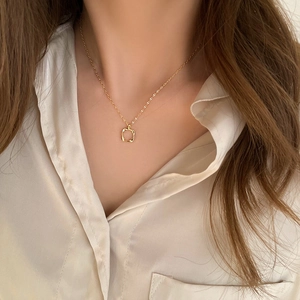 Minimalist gold hollow square pendant necklace for women on a beige shirt background