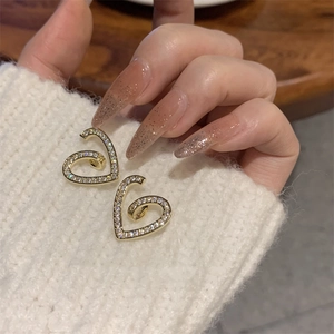 Gros plan sur des boucles d'oreilles cœur dorées avec zircons sur un pull blanc
