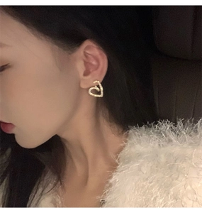 Gros plan de boucles d'oreilles cœur dorées avec pavé de zircons portées à l'oreille