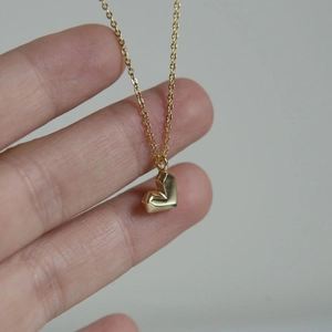 Detaillierte Nahaufnahme einer goldenen Kette mit geometrischem Herzanhänger in der Hand