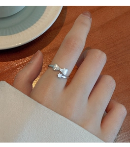 Detail of silver bow ring with shimmering cubic zirconia and floral charm pendant