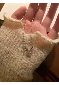 Delicate silver butterfly pendant necklace with heart zircon held in hand over a sweater