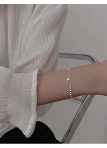Detalle de pulsera de plata con dijes de corazón y candado de corazón brillante en muñeca