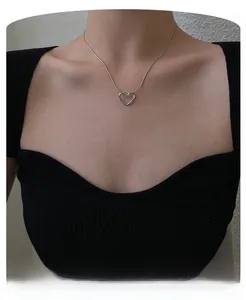 Detail of silver hollow heart pendant on snake chain worn on a black knit top