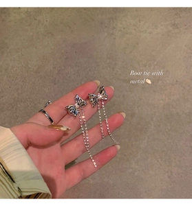 Close-up of silver bow earrings with sparkling rhinestone tassels held by hand