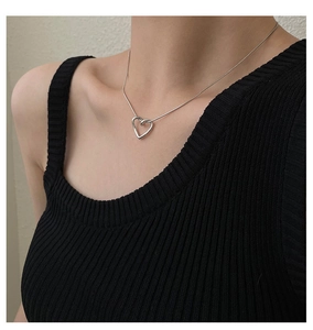 Close-up of silver hollow heart pendant on a sleek snake chain worn by a female model