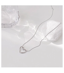 Detail of minimalist hollow heart pendant necklace with sleek snake chain on white surface