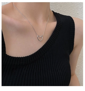 Silver hollow heart necklace on a model's neck with a black knit top and white wall