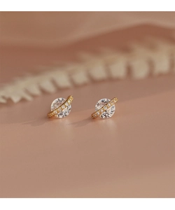 Détail de boucles d'oreilles Saturne en or avec zircons cubiques sur fond beige chaud