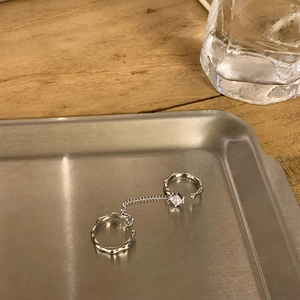 Detailed view of silver chain linked rings featuring a square zircon on wavy metal band