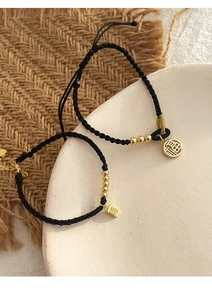 Close-up of black braided cords with golden Fu character pendants and polished beads
